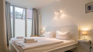 A large bed with white linens, two bedside tables with lamps, a view of the outdoors through a window, and a framed picture on the wall. - App. 02 / EC - Apartment No. 02 in the sunbath (Sassnitz)