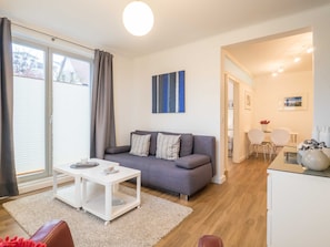 A modern living room with a grey sofa, white coffee table, and a large window with curtains. - App. 02 / EC - Apartment No. 02 in the sunbath (Sassnitz)