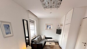 Une pièce de taille modeste comprenant deux lits, un canapé, un téléviseur et un luminaire fixé au plafond.