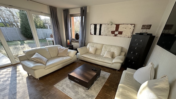 Un salon moderne avec deux canapés en cuir blanc, une table basse en bois foncé et une grande fenêtre agrémentée de rideaux.