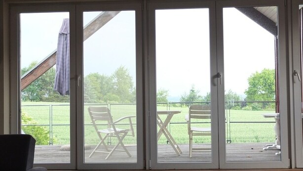 Une pièce dotée d’une porte-fenêtre coulissante donnant sur une terrasse extérieure avec des chaises et une table.
