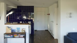 Une cuisine moderne avec des carreaux bleu foncé, une porte blanche et un canapé bleu dans le salon attenant.