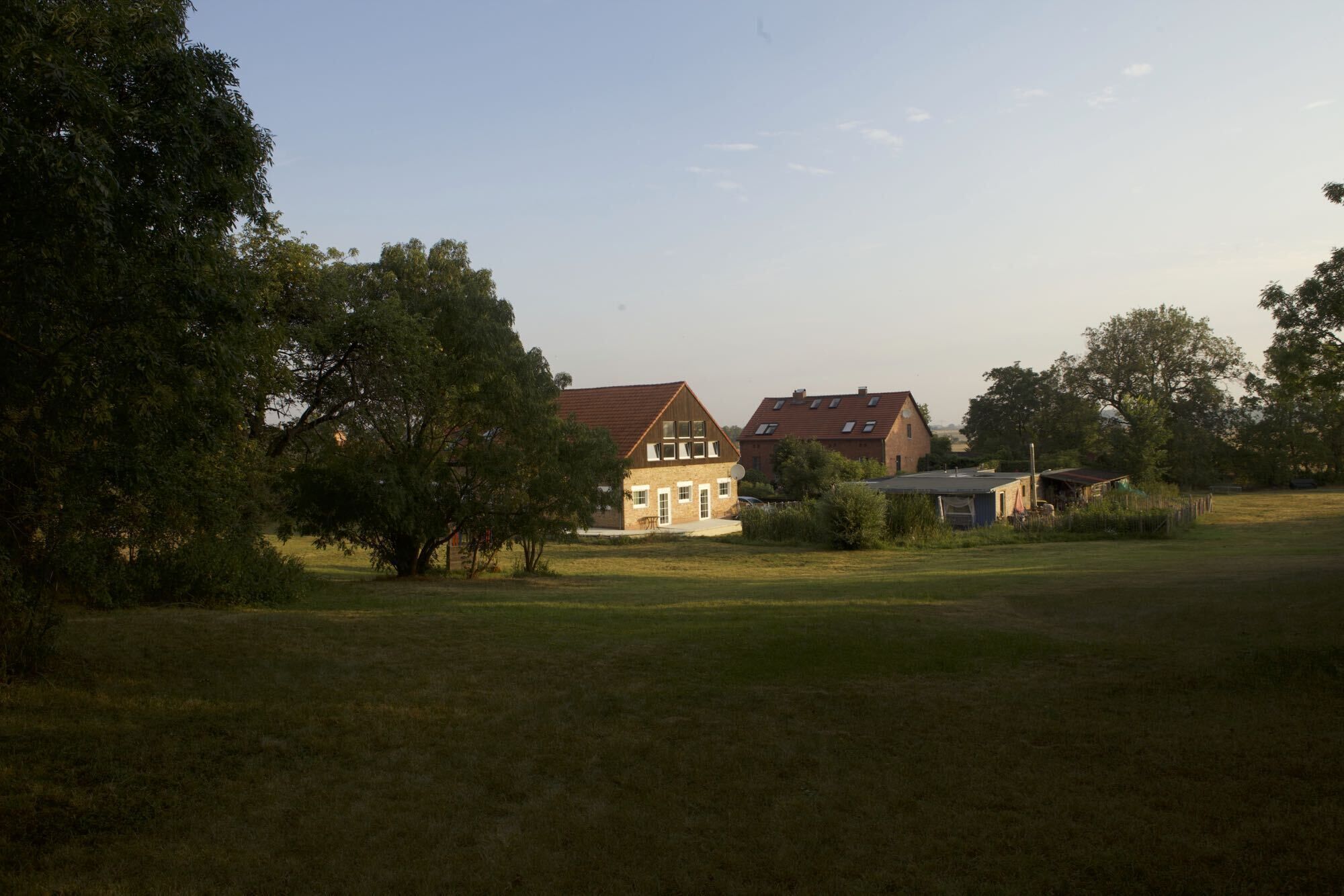 Een groot huis met een rood dak, omringd door een grasveld en bomen.