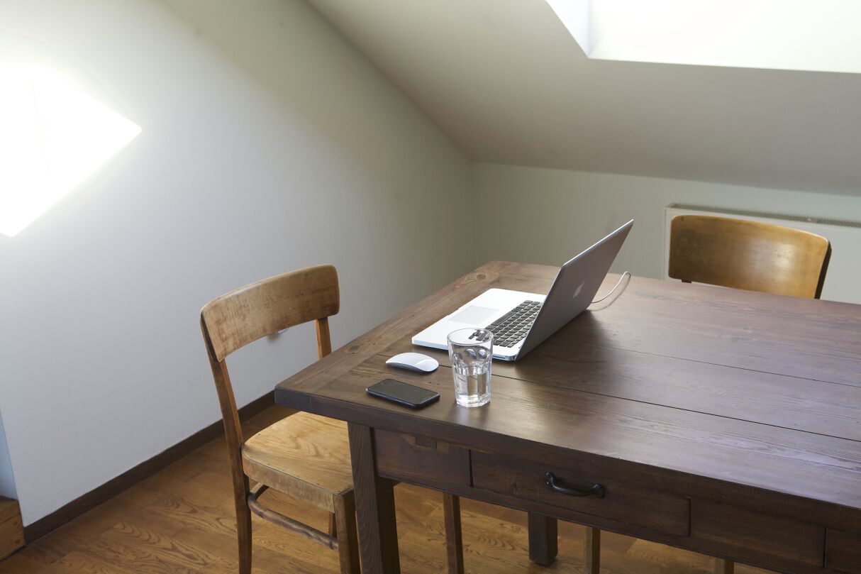 Un tavolo da pranzo in legno con un computer portatile, uno smartphone e un bicchiere d'acqua.