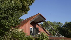 Un bâtiment à toit rouge, doté d’une structure de toit inclinée, entouré d’une végétation luxuriante.