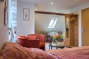 Habitación de hotel con cama, sofá, mesa de comedor con sillas, armario de madera y ventana con vistas.
