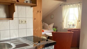 A compact kitchen with a modern stove, wooden cabinets, and a small dining area with a red chair. - Vacation, rest and relaxation in a relaxing natural (Rappin OT Helle)