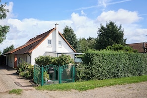 A two-story house with a red-tiled roof, a white exterior, and a green metal gate.