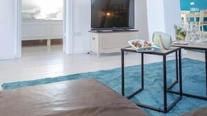 A modern living room with a sofa, a TV on a stand, a dining table with chairs, and a blue carpet. - Vacation apartment Watthof (Emmelsbüll-Horsbüll)