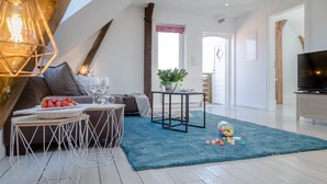 A modern living room with a sofa, coffee table, and TV. There are decorative items like a plant and a basket of fruit. - Vacation apartment Watthof (Emmelsbüll-Horsbüll)