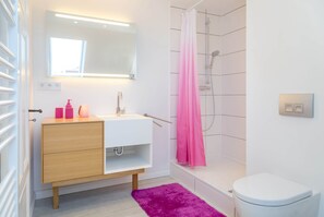 Une salle de bain moderne avec un lavabo blanc, un meuble-lavabo en bois, un rideau de douche rose et des toilettes blanches.
