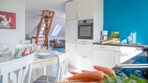 A modern kitchen with white cabinets, a blue accent wall, and a dining area with a table set for two. - Vacation apartment Watthof (Emmelsbüll-Horsbüll)