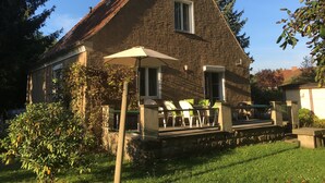Une maison en pierre avec un toit en pente, une cheminée et un porche doté de sièges pour l’extérieur.