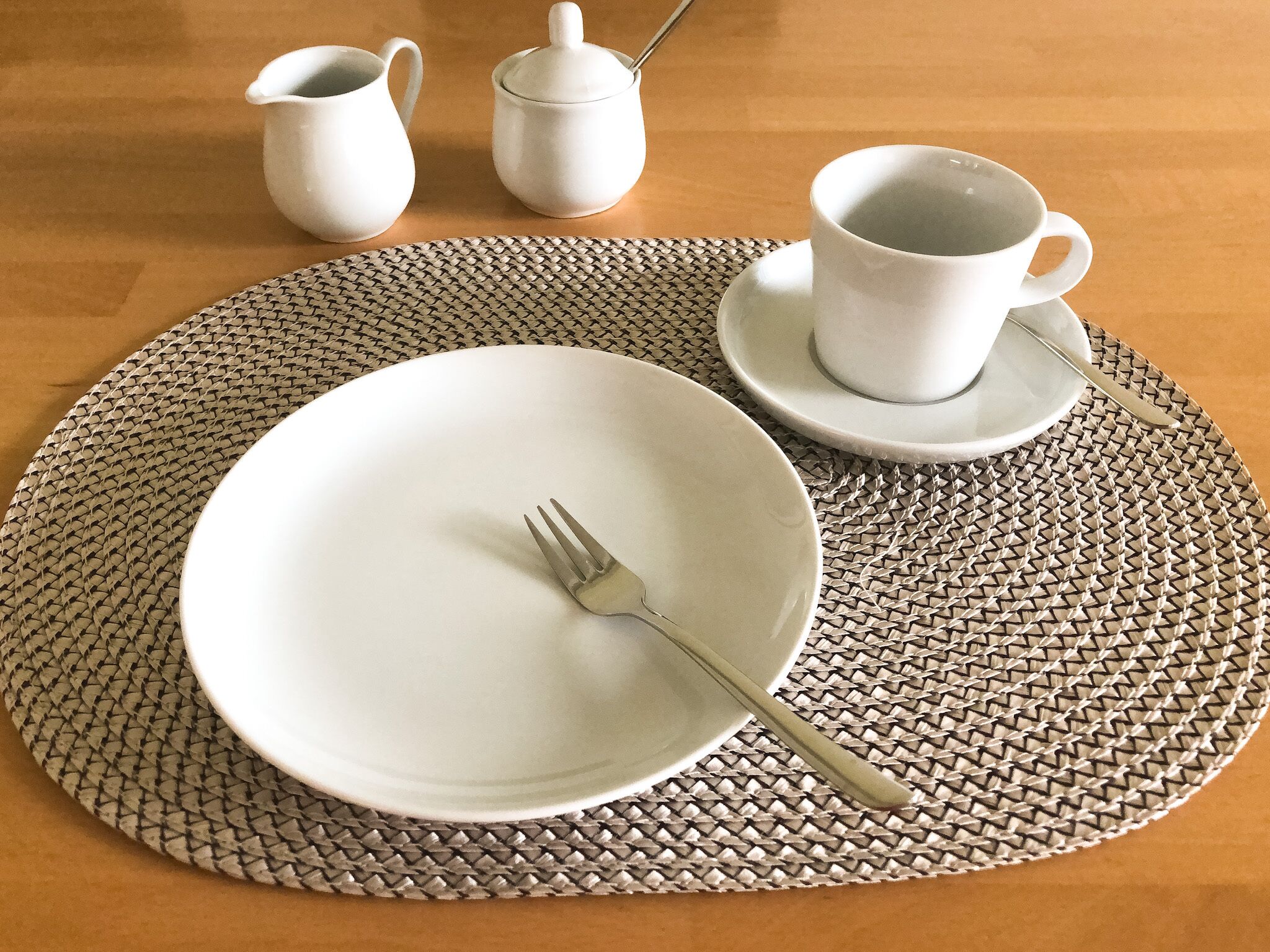 A table set with a white plate, a fork, a cup and saucer, a pitcher, and a salt and pepper shaker.