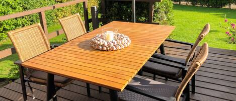 Une terrasse en bois avec une table et des chaises, entourée de verdure.