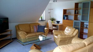 Ein Wohnzimmer mit einer Couch, einem Sessel, einem Glastisch und einem Bücherregal.
