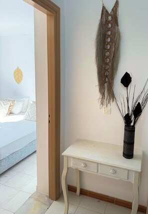 A room with a bed, a desk with drawers, and a wall-mounted macrame piece.