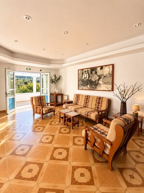 A spacious lobby with a geometric patterned floor, a seating area with sofas and chairs, a painting on the wall, and a view through the open door.