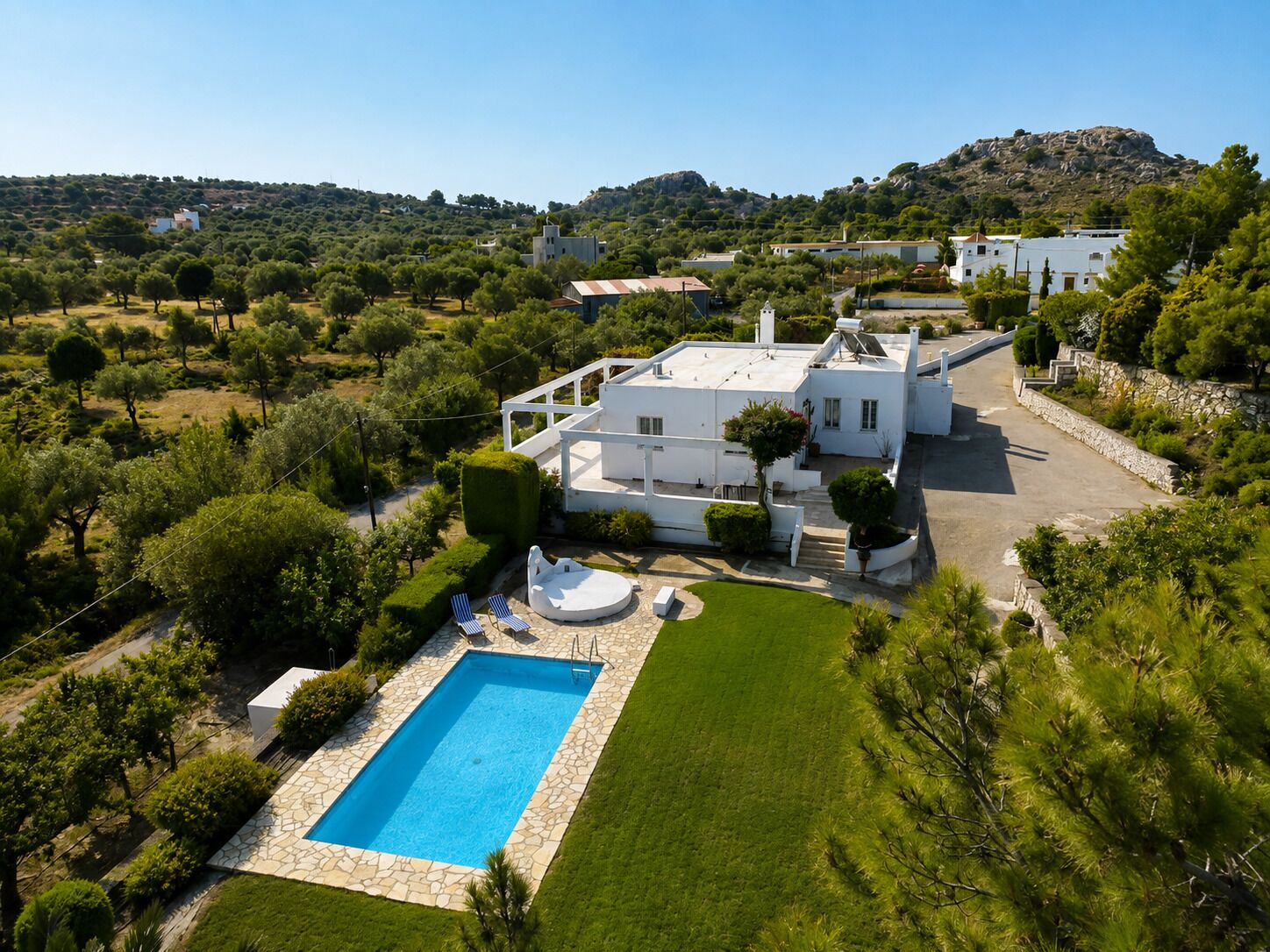 Una villa bianca con piscina, immersa nel verde e circondata da colline.