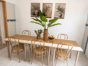 A dining area with a long wooden table, six wicker chairs, and a potted plant in the center.