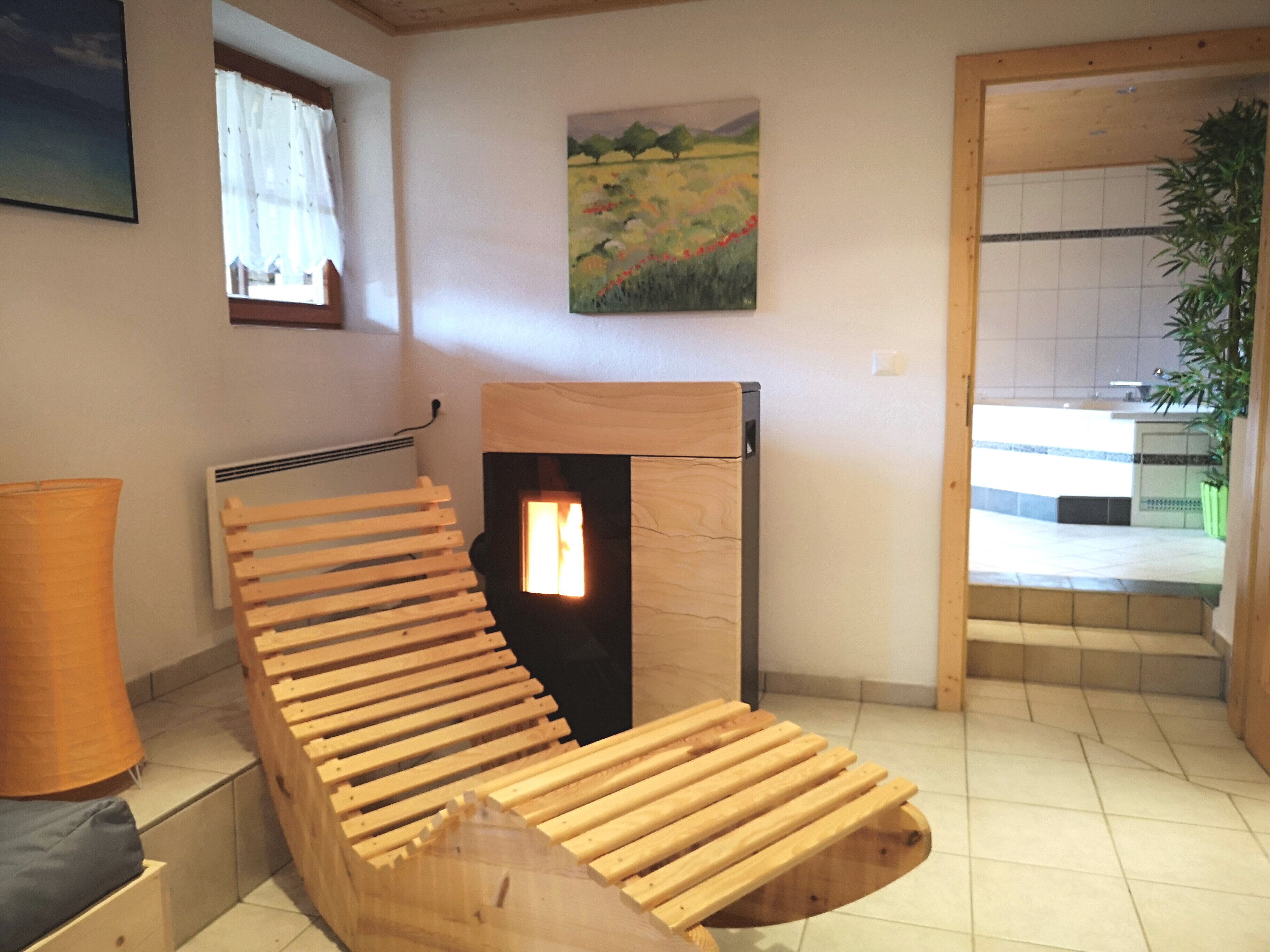 A room with a wooden bench, a fireplace, a painting, and a view of the outside.
