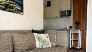 A living room with a brown sofa, a patterned throw pillow, and a kitchen area with wooden cabinets and a microwave. - 5min beach & forest, sunny, single storey (Prerow)