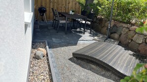 An outdoor patio area with a table and chairs, a barbecue grill, and a covered seating area. - 5min beach & forest, sunny, single storey (Prerow)