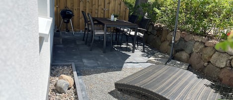 Un espace extérieur aménagé avec une table et des chaises, un barbecue et un coin salon abrité.