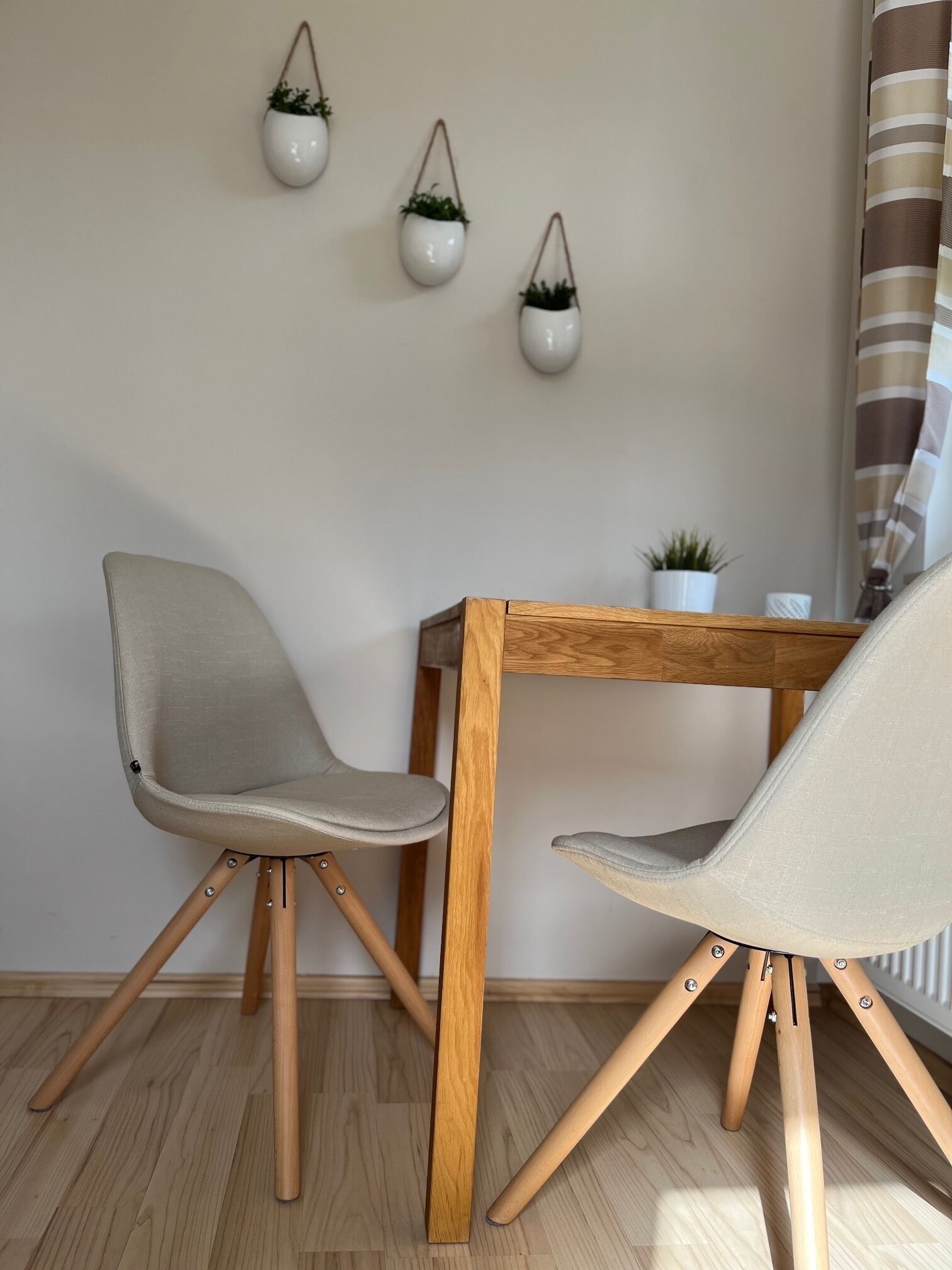 A room with two chairs and a small table, wooden floor, and three hanging planters on the wall.