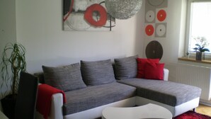 A modern living room with a grey sectional sofa, a white coffee table, and a red throw blanket. - Free mobility with public transport! (Zell am see)