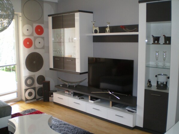 A modern living room with a flat-screen TV, built-in shelves, and a glass cabinet. - Free mobility with public transport! (Zell am see)