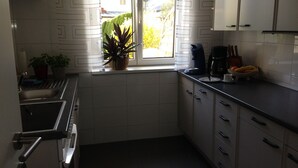 A compact kitchen with white cabinets, a stainless steel sink, and a window with a view of a house and greenery outside. - Free mobility with public transport! (Zell am see)
