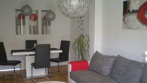 A modern living room with a grey sofa, a white coffee table, and black chairs. There is a dining table with chairs and a hanging light fixture. - Free mobility with public transport! (Zell am see)