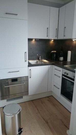 Una cocina moderna con armarios blancos, electrodomésticos de acero inoxidable, un lavamanos y un cubo de basura.