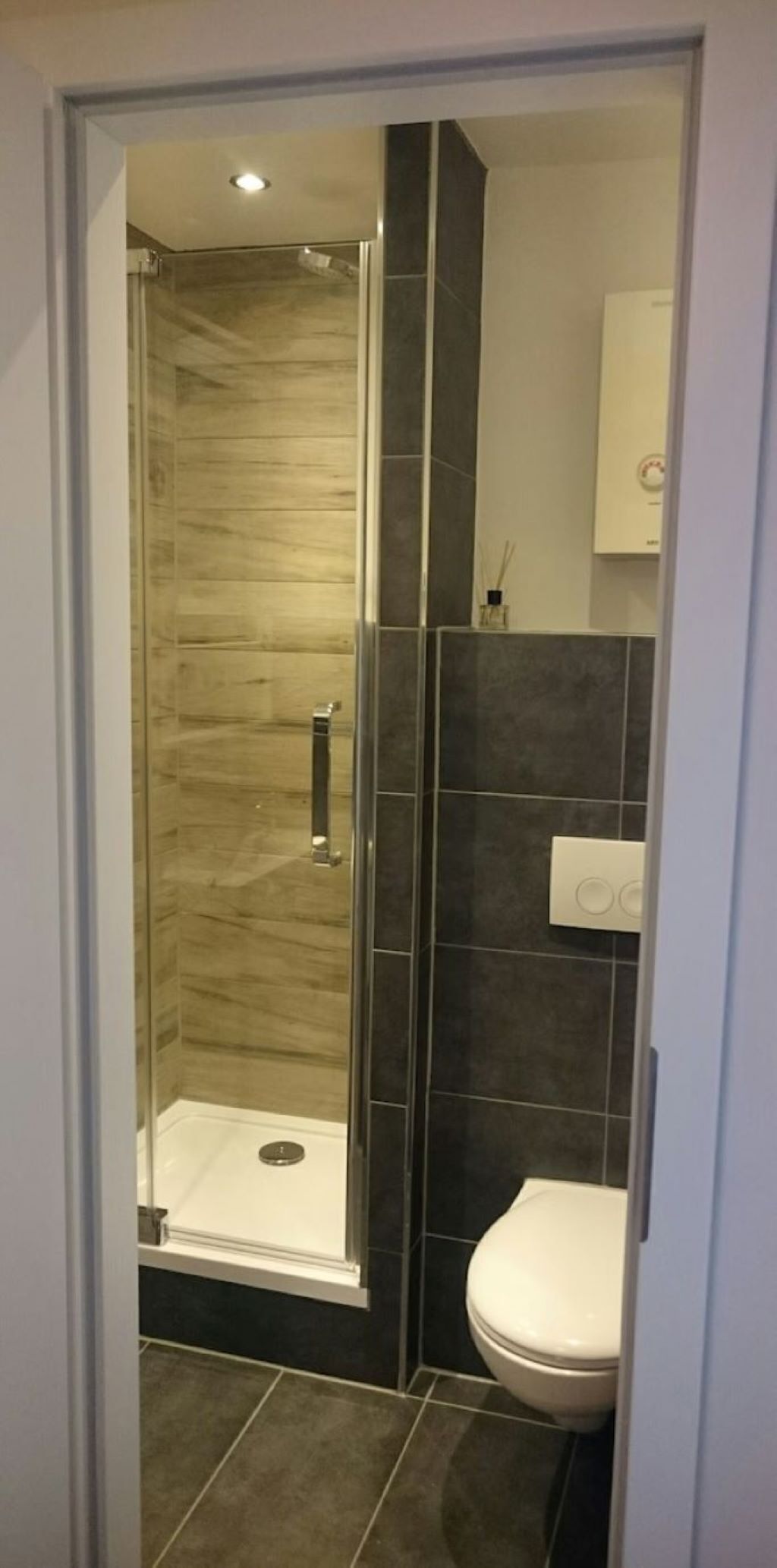 Et moderne badeværelse med en glasafskærmet brusekabine, mørke flisevægge og et hvidt toilet.