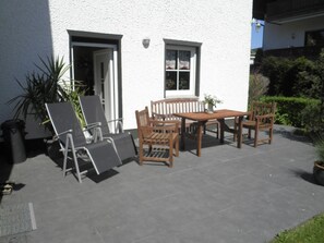 An outdoor patio with a wooden table and chairs, a potted plant, and a trash bin. - ☀️☀️☀️ cozy apartment with additional room to expand (Willingen)