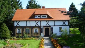Ein traditionelles Fachwerkhäuschen mit rotem Ziegeldach, einer Haustür und einem Garten mit gepflastertem Weg und Blumenbeeten.
