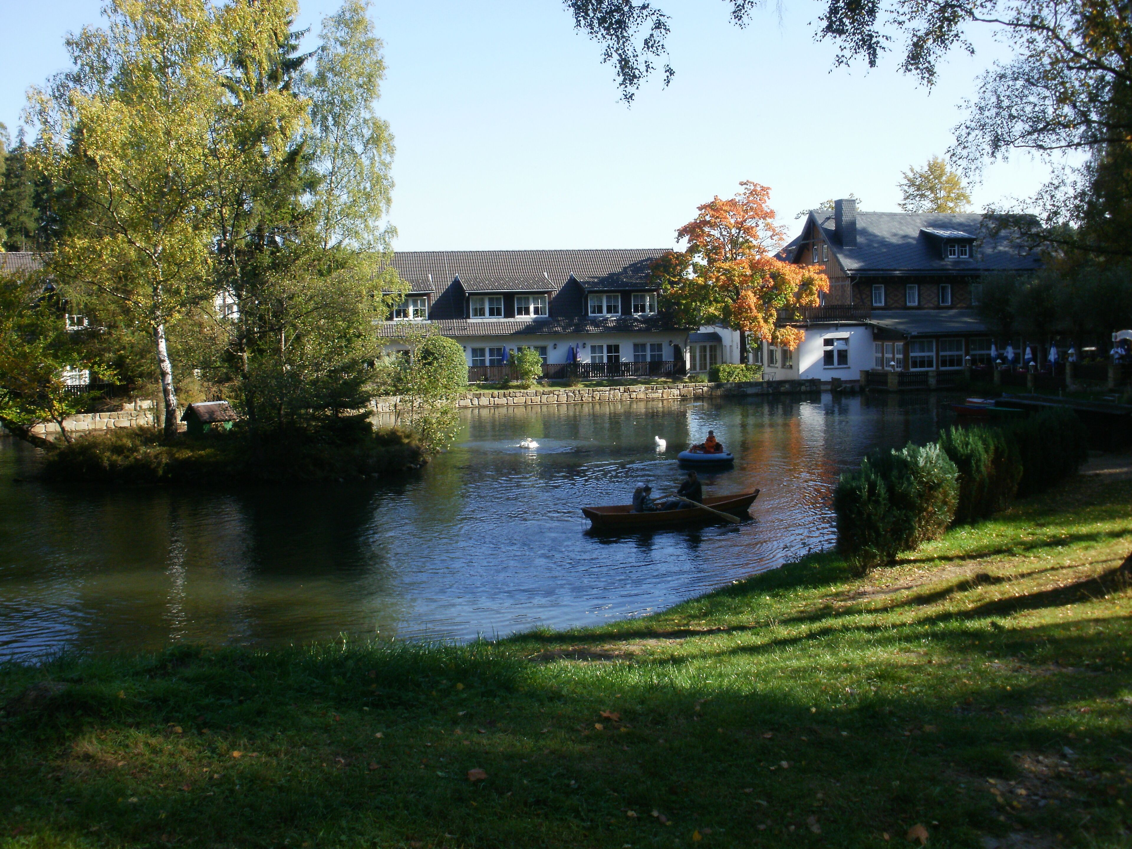 Ein Fluss mit Booten, eine grüne Uferbank und Häuser im Hintergrund.