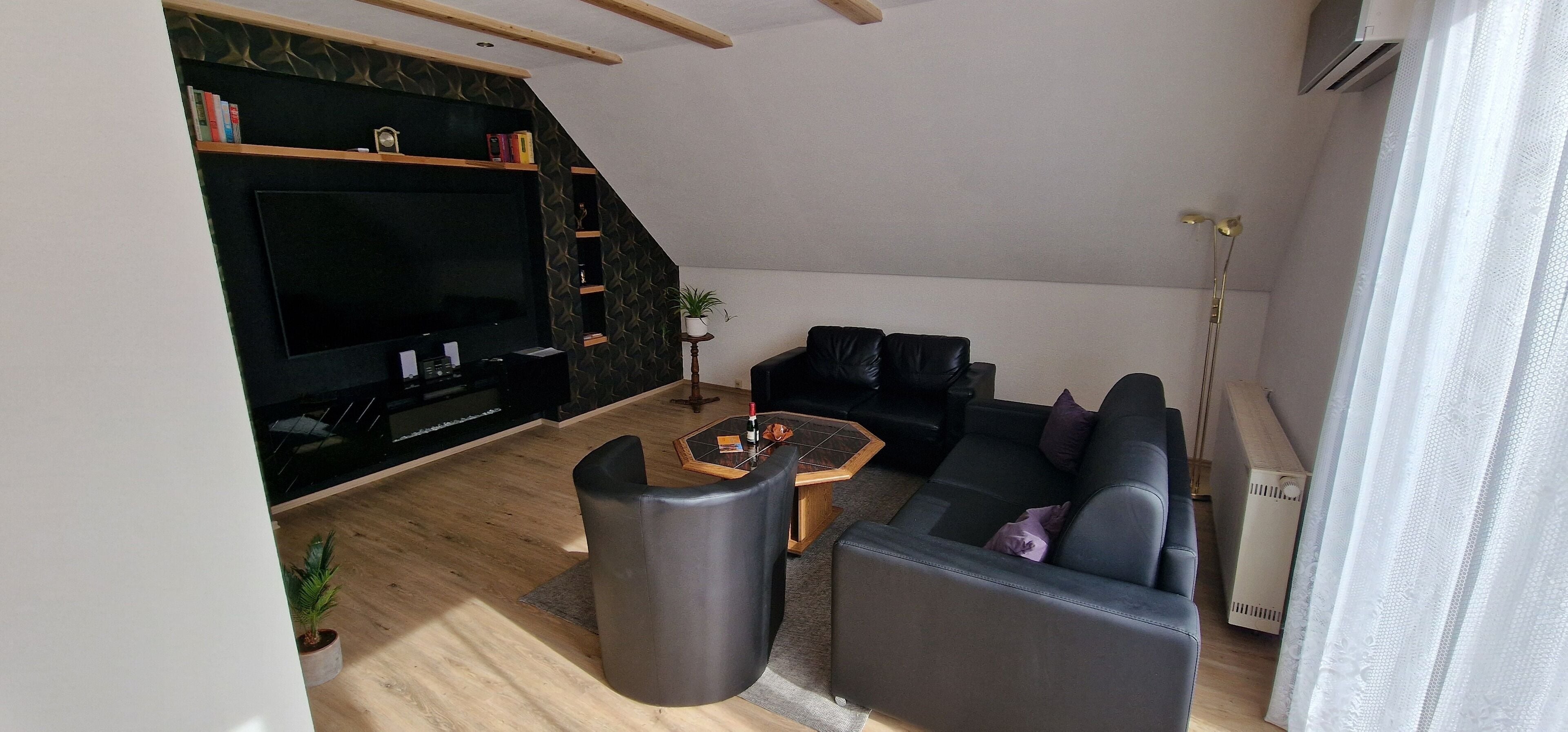 Ein modernes Wohnzimmer mit Flachbildfernseher, einer schwarzen Ledersofa, einem Couchtisch und einer Treppe, die zu einer oberen Ebene führt.