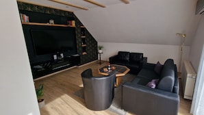 Ein modernes Wohnzimmer mit Flachbildfernseher, einer schwarzen Ledersofa, einem Couchtisch und einer Treppe, die zu einer oberen Ebene führt.