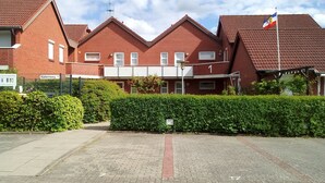 A row of red brick houses with a flag, a paved driveway, and a hedge. - Renovated 2-room apartment, bright and friendly, dogs are welcome (Schönberg)
