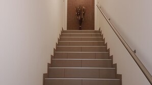 Un escalier avec une rampe, un luminaire fixé au mur et un vase contenant des fleurs séchées, le tout situé en haut de l’escalier.