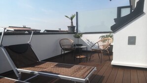 Une terrasse sur le toit avec un transat, deux fauteuils en osier, une petite table et des plantes en pot.