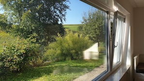 A room with a large window overlooking a grassy area with trees and a clear sky. - Quiet 67 m² apartment in the beautiful green of Bad Urach (Bad Urach)