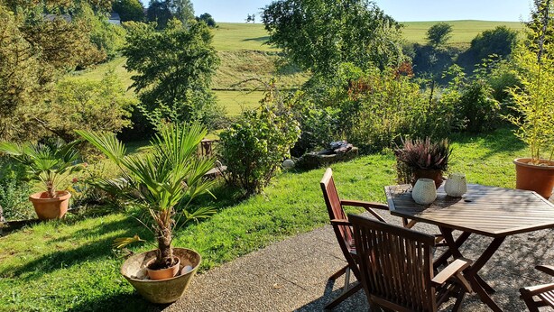 An outdoor patio with a wooden table and chairs, surrounded by potted plants and a gravel path. - Quiet 67 m² apartment in the beautiful green of Bad Urach (Bad Urach)