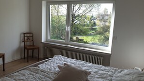 A bedroom with a large window, a bed, a radiator, and two wooden chairs. - Quiet 67 m² apartment in the beautiful green of Bad Urach (Bad Urach)