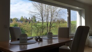 A dining area with a view of a green landscape through large windows. - Quiet 67 m² apartment in the beautiful green of Bad Urach (Bad Urach)