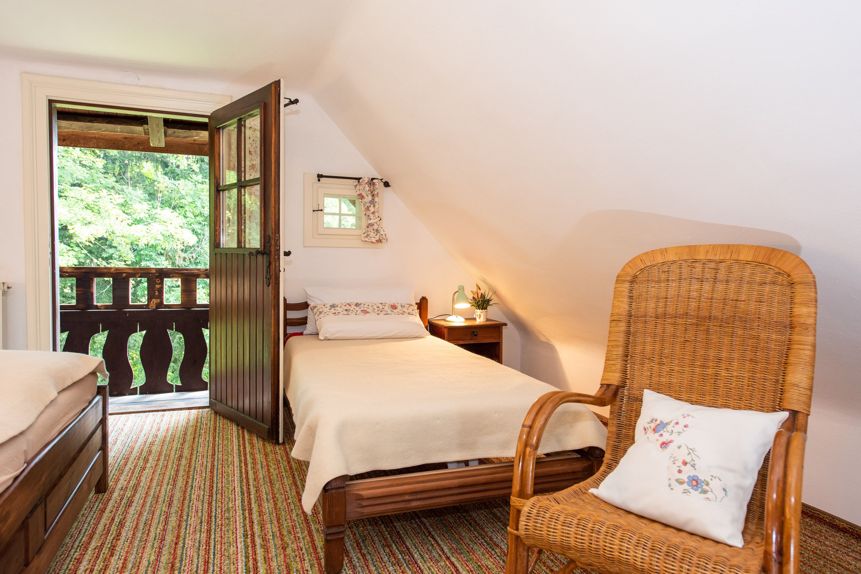 A bedroom with a bed, a chair, a nightstand, and a window with a view of greenery.