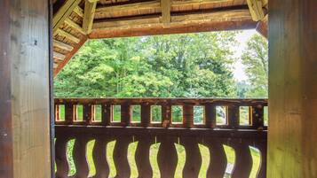 A wooden structure with a sloped roof and a view of a forested area through a windowed railing.