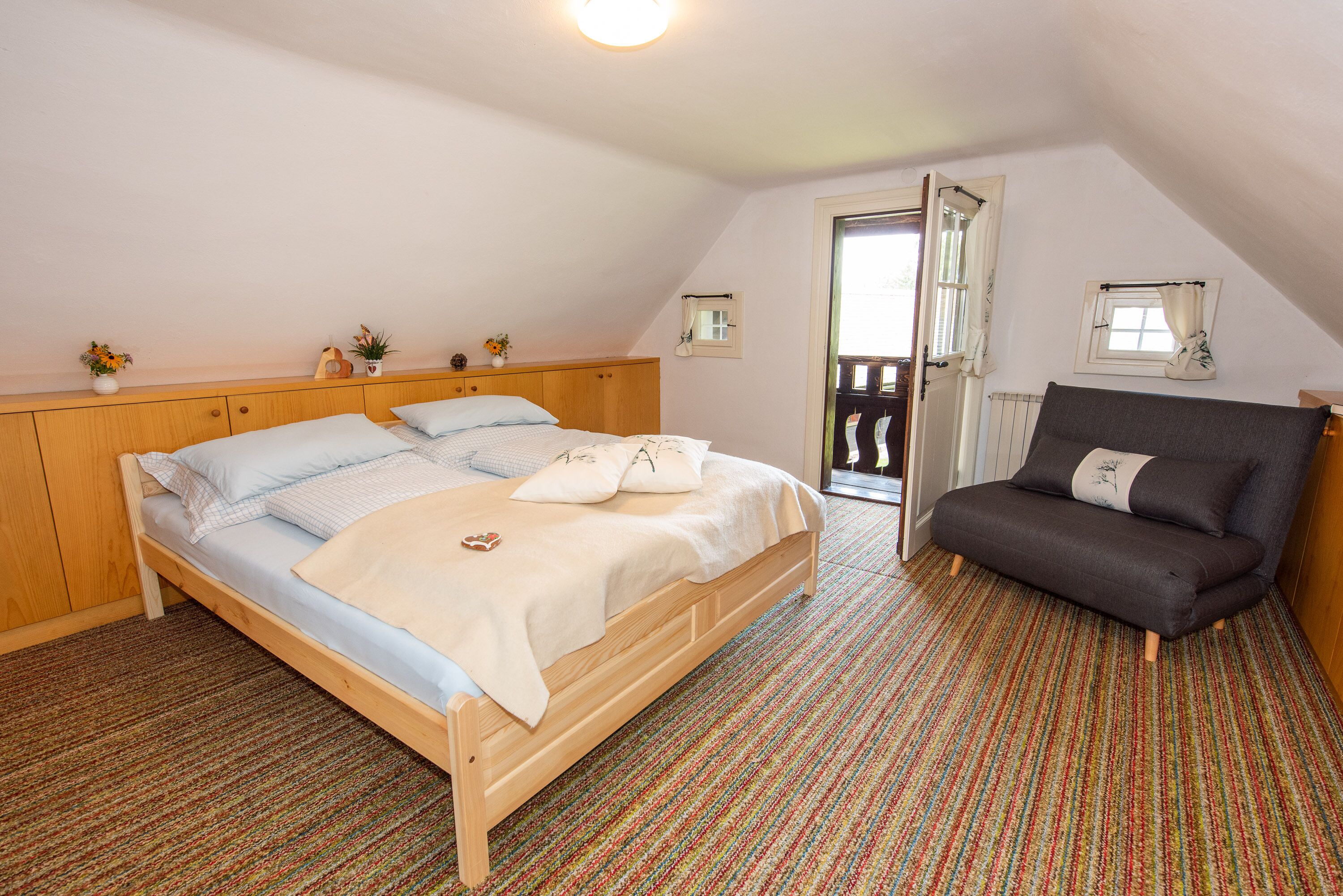 Ein Schlafzimmer mit einem hölzernen Bett, einem grauen Sofa und einem bunten Streifen Teppich.
